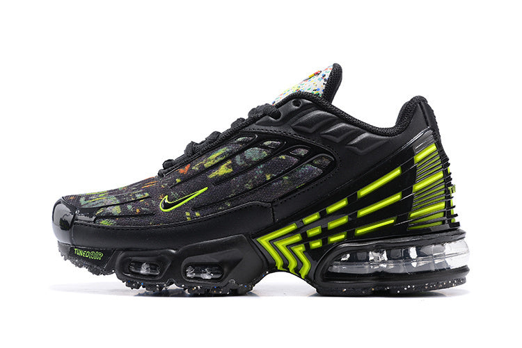 Side view of a black Nike sneaker with multicolored splatter detailing, bright volt accents, a sculpted side cage, and visible cushioning.