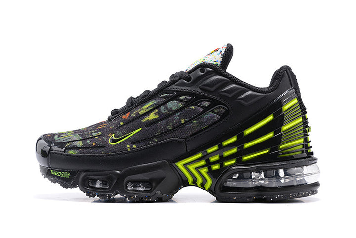 Side view of a black Nike sneaker with multicolored splatter detailing, bright volt accents, a sculpted side cage, and visible cushioning.