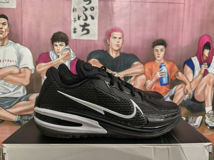 Side view of black Nike basketball sneakers with a white Swoosh and layered black-and-white outsole on a shoe box.