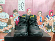 Front view of black high-top basketball shoes with gold Under Armour logos on the tongues.