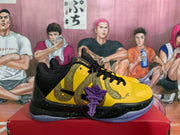 Side view of a yellow sneaker with gold snake-themed detailing, black overlays, a speckled midsole, translucent outsole, and purple lace accessory.
