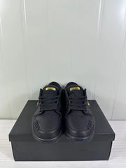 Front view of a black low-top sneaker pair with gold-tone tongue details and perforated toe areas.