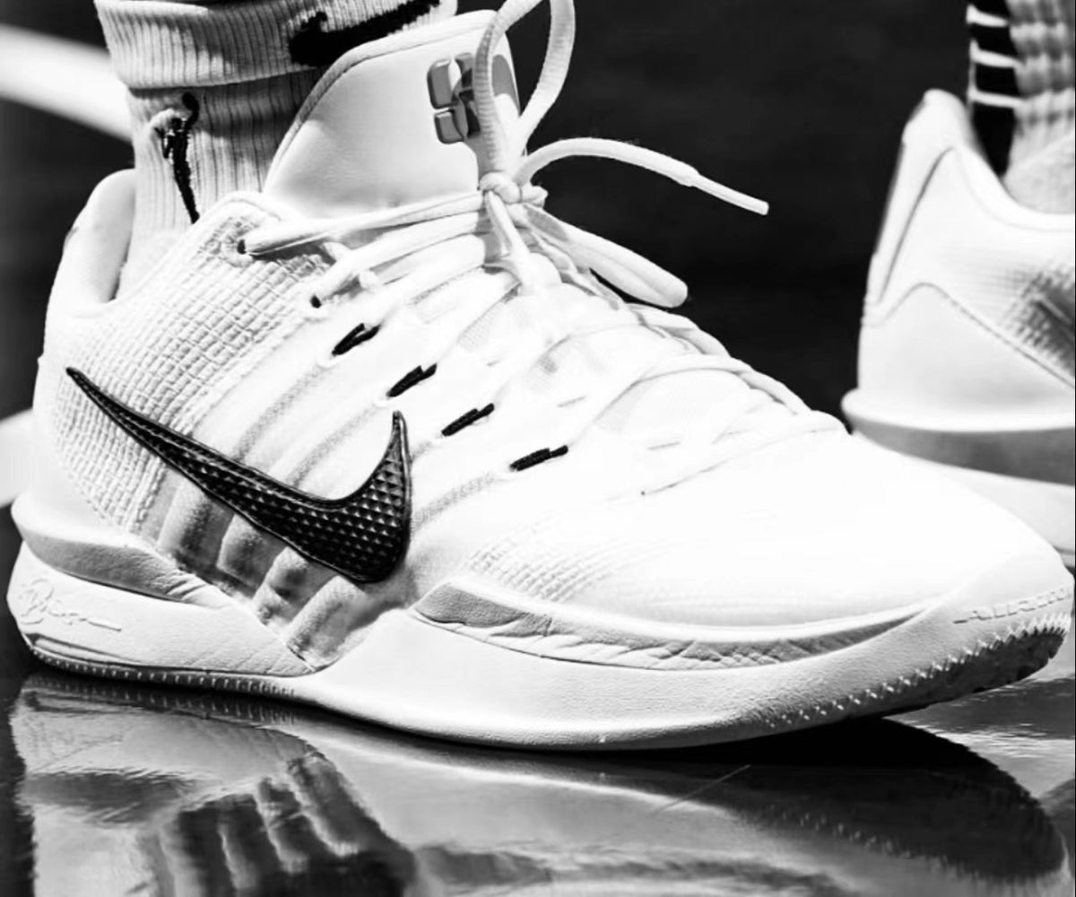 Close-up of white and black high-top sneakers with a black Swoosh-style side mark, white laces, padded collar and textured outsole.