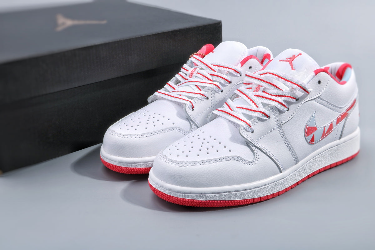 Pair of white low-top Jordan sneakers with pink-red accents, patterned side swooshes, and red outsoles beside a black shoebox.