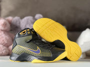 Pair of sneakers showing the patterned black upper, purple Swoosh, and yellow textured outsoles.