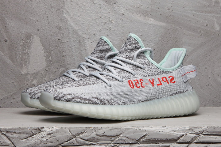 Side view of a gray and white Yeezy 350 V2 sneaker with red side lettering, mint collar accents, and a translucent ribbed sole.