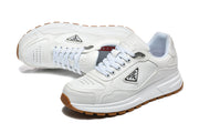 Angled view of white Prada low-top sneakers with perforated toe panels and gum-colored soles.