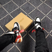 Worn view of the sneakers beside a tan shoebox, with black and orange details visible.