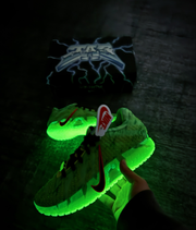 Glowing green sneakers held in front of the matching black graphic box.