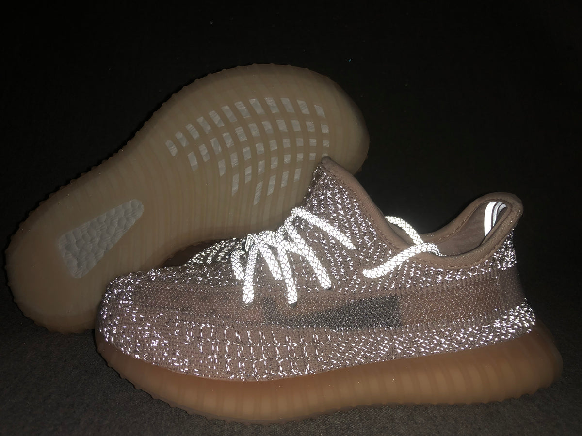 Close-up of the light gray and pink-toned sneaker with reflective-looking laces and a translucent gum-colored sole.