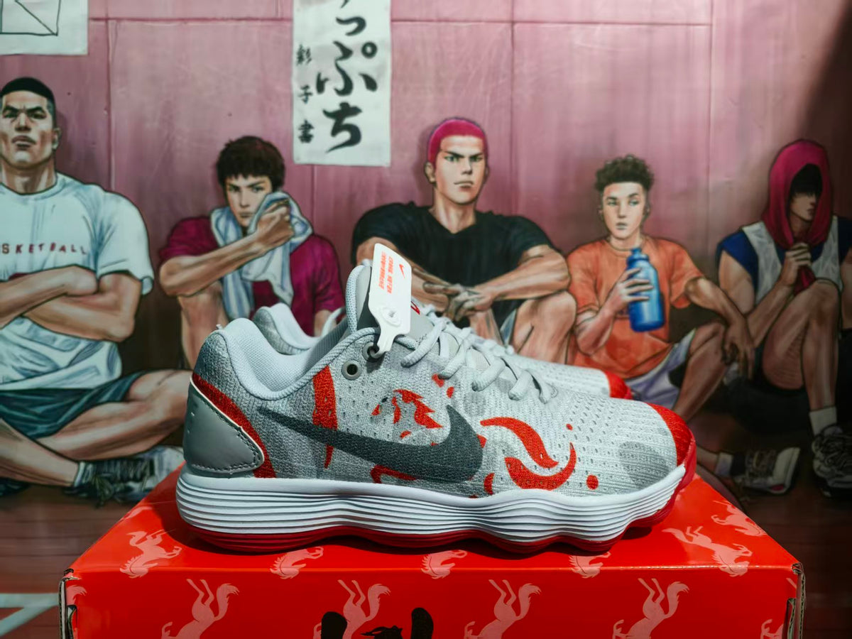 Side view of grey and red Nike basketball sneakers with a dark Swoosh, displayed on a red patterned box.
