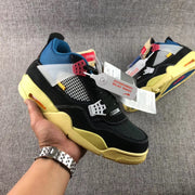 Handheld side view of a black sneaker showing the white mesh panel, translucent side piece, red hardware, and yellow-toned sole.