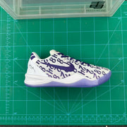 Side profile of a white and purple basketball sneaker displayed on a green cutting mat.