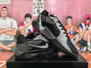 Angled display of the black and grey Nike basketball sneakers, showing the side branding, patterned panels, black midsoles, and rubber outsoles.