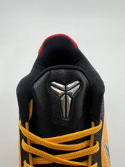 Close-up of the black tongue, metallic Kobe logo, and yellow-orange laces.
