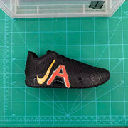 Side view of a black basketball shoe with red-orange graphic and gold-colored Swoosh