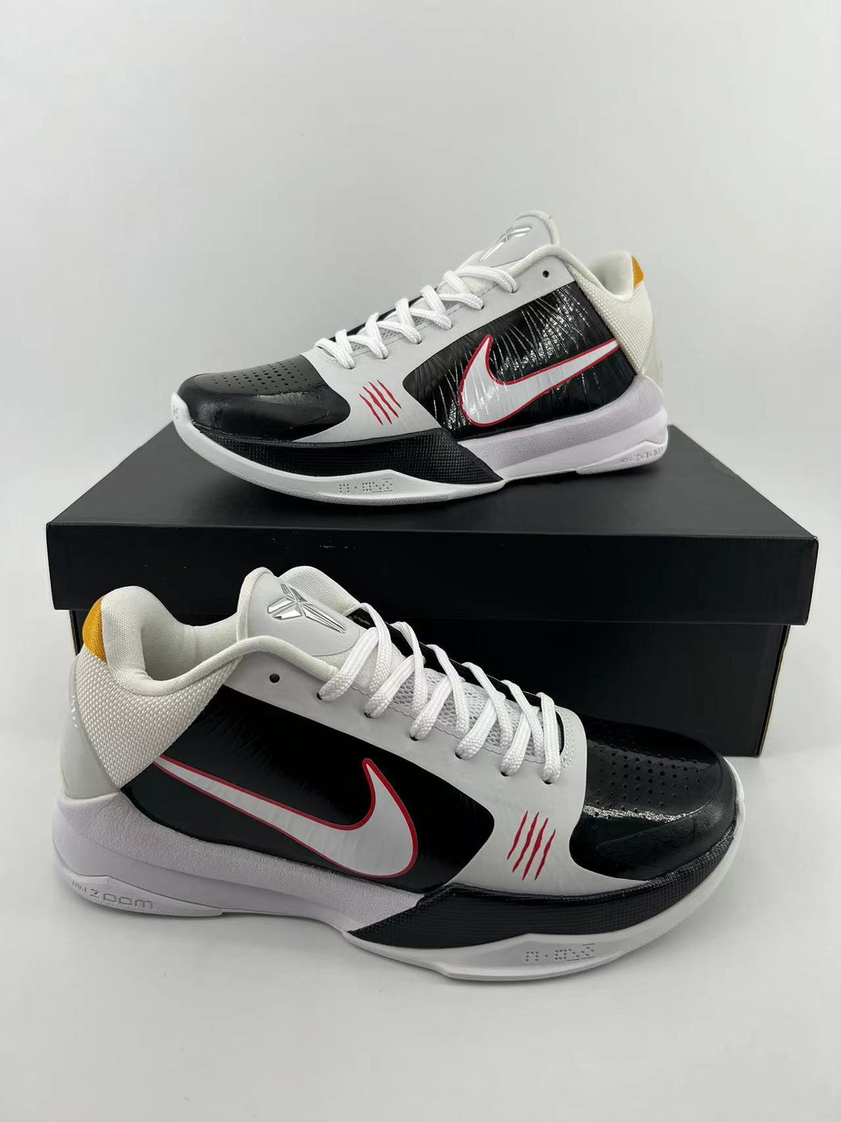 Pair of low-top Nike Kobe basketball shoes in white, black, and red, displayed on a black box