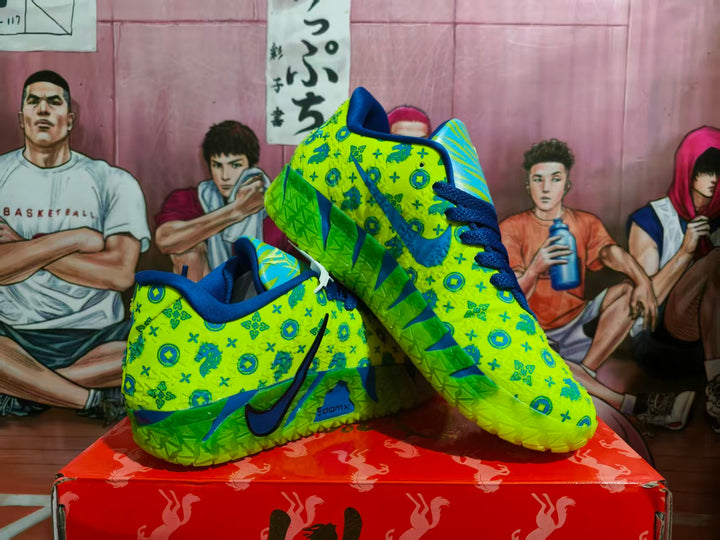 Pair of yellow and blue Nike sneakers with a patterned upper, blue laces, and textured green soles shown from an angled side view.