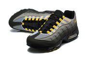 Pair of grey Nike Air Max 95 TT sneakers with yellow lace details and black soles.