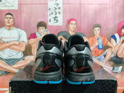 Rear view of the black basketball sneakers showing gray heel panels, glossy black details, blue outsole edges, and red heel graphics.