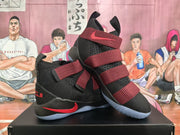 Three-quarter view highlighting the high-top shape, layered straps, red side accents, and textured black upper.