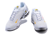 Front view of white Nike Air Max Plus sneakers with yellow accents and lace-up closures.