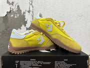 Pair of yellow Converse training-style shoes displayed at an angle, showing the side emblems and textured gum-colored soles.