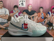 Side view of a white Nike basketball sneaker showing the perforated upper, light blue-green toe accent, NBA hangtag, and ZoomX midsole branding.