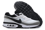 Side view of white, black, and grey Nike Air Max sneakers, with one shoe turned over to show the treaded outsole.