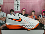 Side profile of a white Nike basketball shoe with orange accents, a patterned outsole, and visible Air Zoom text.