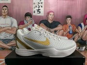 Side view of a white Nike basketball sneaker with a textured upper, gold Swoosh and Zoom branding on the sole.