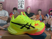 Side view of a lemon-yellow ASICS basketball shoe with black branding, mesh-like upper details, and orange-red sole accents.