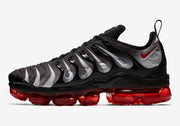 Side view of a Nike Air VaporMax Plus sneaker showing the red heel Swoosh and translucent red sole.