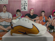 Side profile showing the white perforated upper, gold side overlay, purple trim, and textured outsole.