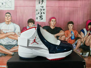 Side profile showing the ankle strap, white textured upper, dark blue overlays, and red outsole detailing.