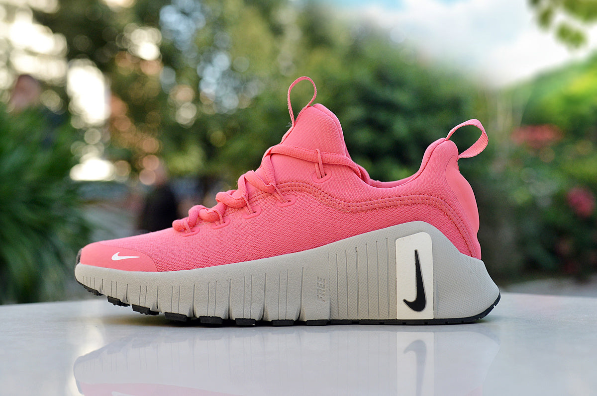 Side view of a pink Nike low-top sneaker with a lace-up upper, pull tabs, and a thick grooved white sole.
