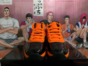 Front view of black and orange high-top basketball sneakers with orange laces and glossy black toe panels.