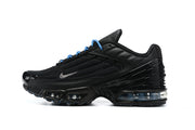 Side profile of a black Nike Air Max Plus sneaker with blue lace accents and visible sole cushioning.