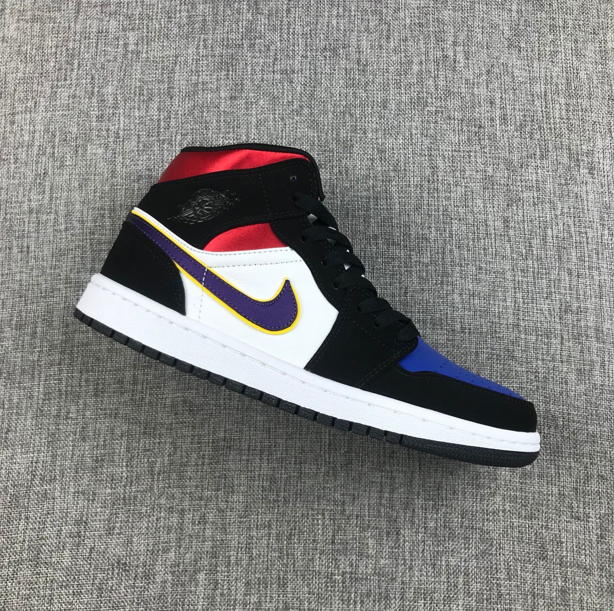 Side view of a black, white, purple, yellow, blue, and red Jordan 1 Mid sneaker.