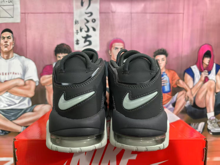 Rear view of black Nike basketball sneakers with grey-green swoosh accents, translucent sole windows, and light outsoles on a Nike box.