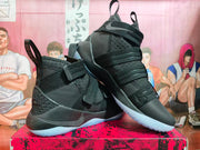 Angled side view of black strap-closure high-top basketball shoes with light blue outsoles.