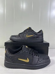 Angled product view showing the black sneaker pair, gold-tone side branding, perforated toes, and lace-up construction.
