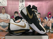 Two Nike basketball sneakers displayed together, showing contrasting black and white uppers, gold accents, and textured outsoles.