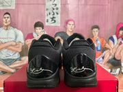 Rear view of the black sneakers showing glossy heel panels and contrasting signature-style graphics.