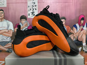 Angled view showing the orange outsole sections, black upper, heel details, and lace loops.