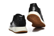Rear and outsole views of black sneakers with off-white midsoles and gum-colored tread.