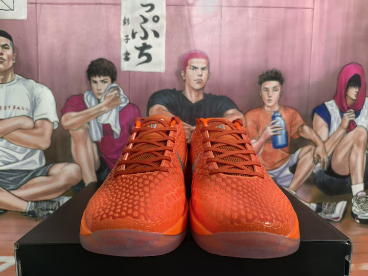 Pair of bright orange Nike basketball sneakers shown from the front on a black shoe box.