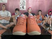 Front view of the pair showing coral-orange textured toes, pink tongues and collars, orange laces, and green tongue logos.