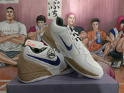 Angled view of the white and tan Nike basketball sneakers highlighting the blue Swoosh, lace-up construction, and speckled midsole.