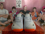 Front view of white Nike basketball sneakers with black toe branding, gray laces, and bright orange outsoles.